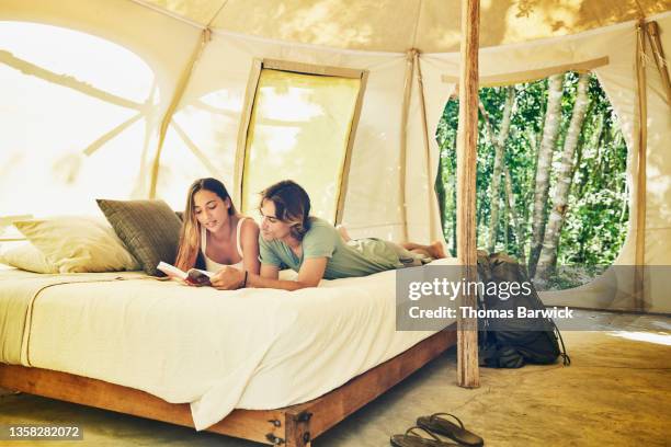 wide shot of couple reading on bed in tent while staying at eco resort in jungle - staying indoors stock pictures, royalty-free photos & images