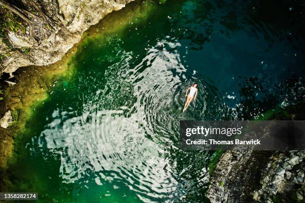 extreme wide shot aerial view of woman floating on back in cenote in jungle - harmony ストックフォトと画像