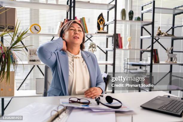 woman sitting at desk and having neck pain, she is touching her neck - person with a neck pain stock pictures, royalty-free photos & images