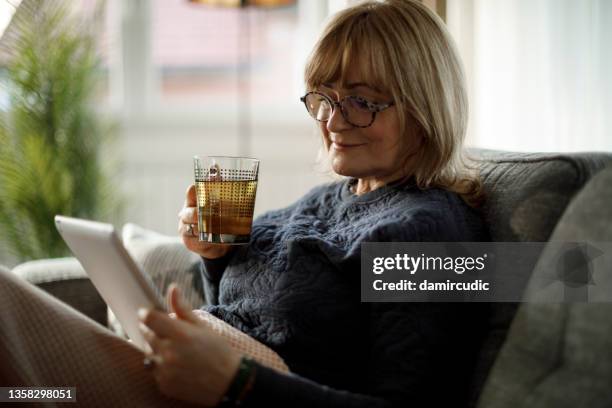 porträt einer lächelnden reifen frau mit digitalem tablet und tee trinken zu hause - grüner tee stock-fotos und bilder