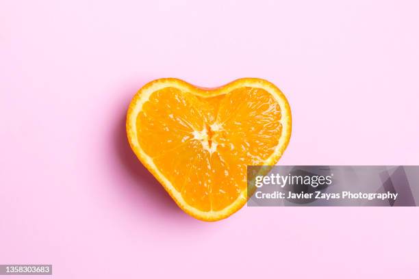 heart shaped orange half on pink background - halved stock-fotos und bilder