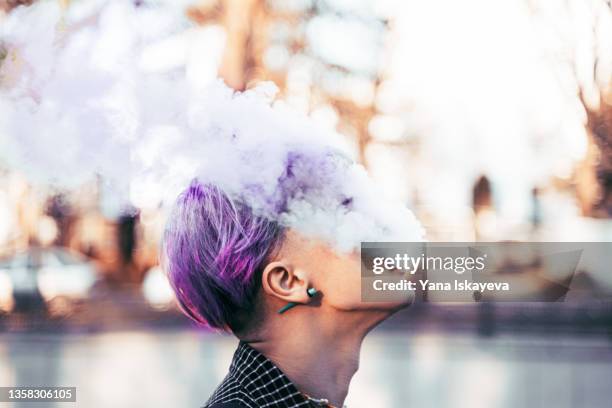 young hipster with purple, very peri colored hair is smoking vape - quit smoking stockfoto's en -beelden