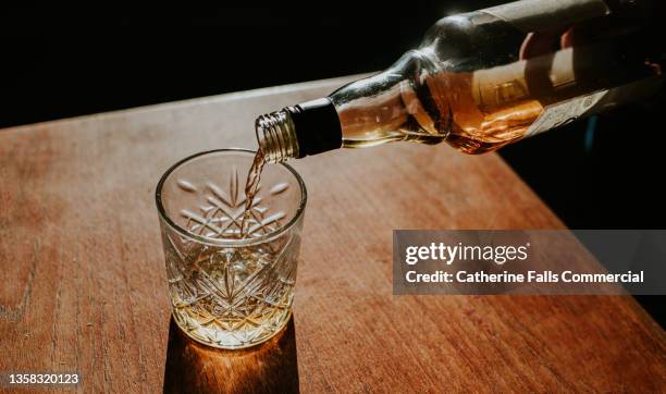 whisky pour from a bottle into a cut glass tumbler - cognac stockfoto's en -beelden