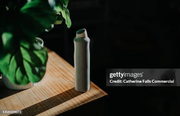 an unbranded anti-perspirant casting a shadow on a wooden table beside a plant - aerosol stock pictures, royalty-free photos & images