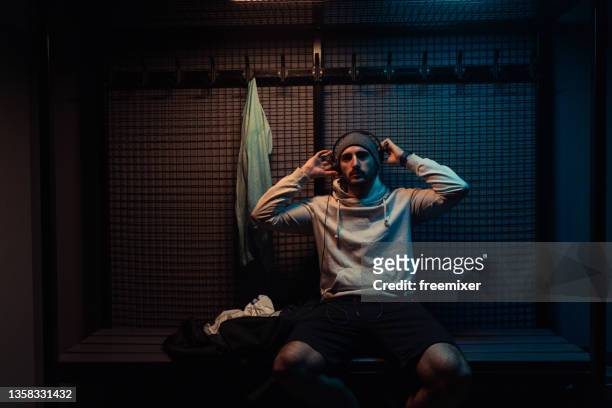 jovem de camisa encapuzada com fones de ouvido sentado em camarim de academia - hoodie headphones - fotografias e filmes do acervo