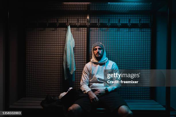 joven con camisa encapuchada sentado en el vestuario del gimnasio - gym bag fotografías e imágenes de stock