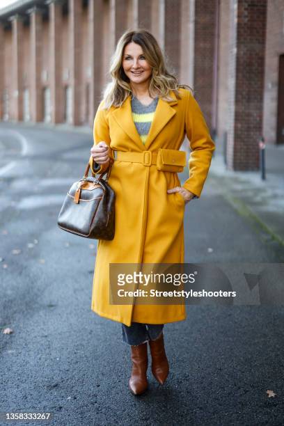 Host Frauke Ludowig wearing a long yellow coat by Miss Goodlife, a grey and yellow fuzzy knitted pullover by Miss Goodlife, grey denim jeans pants by...