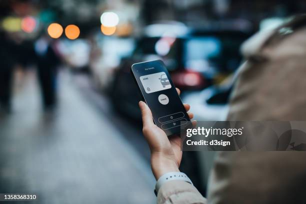 over the shoulder view of young asian woman using mobile app device on smartphone to unlock the doors of her intelligence car in city street. wireless and modern technology concept - mobile app car stock pictures, royalty-free photos & images