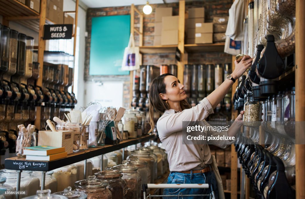 Shot of a young woman filling a jar with product while shopping