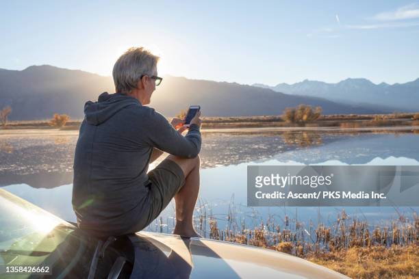 man relaxes on car hood, looks out to sunrise - gray shorts stock pictures, royalty-free photos & images