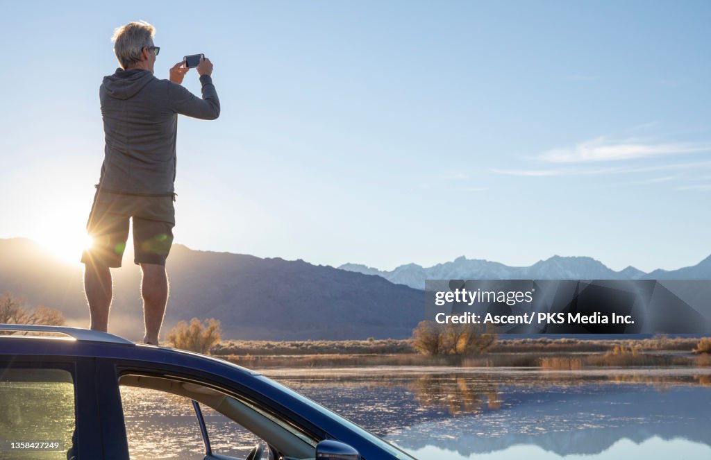 Man relaxes on car hood, looks out to sunrise