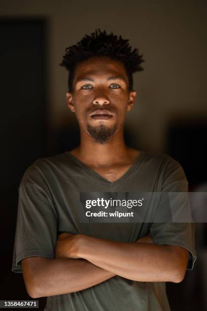 ritratto serio di giovane maschio di razza mista con gli occhi verdi e le braccia dei capelli rasta incrociate - occhi verdi foto e immagini stock