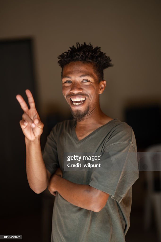 Signe de paix Portrait d’un jeune homme métis aux yeux verts et aux cheveux rasta souriant en regardant la caméra