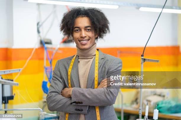 portrait of young smiling african american professional fashion designer, with tape measure on his neck, standing in his  workplace. new business opportunity in fashion industry and small business concept. - modeontwerper stockfoto's en -beelden