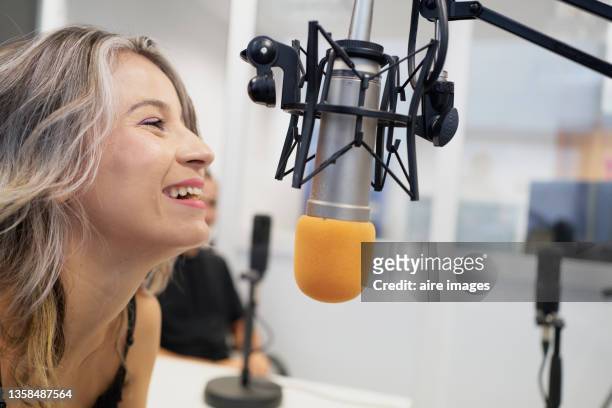 side view of beautiful presenter wearing black clothes sitting in front of the microphone very smiling while speaking to the audience during a radio show - microphone desk fotografías e imágenes de stock