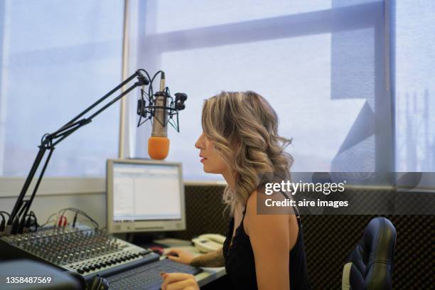 side view of unrecognizable female presenter with blonde hair sitting in radio studio in front of microphone during her radio show - radio station fotografías e imágenes de stock