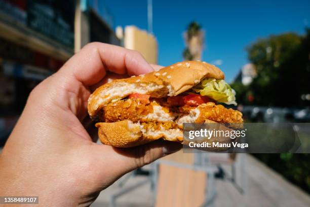 close up view of man holding chicken burger, in background blurred image of city. - little burger stock pictures, royalty-free photos & images