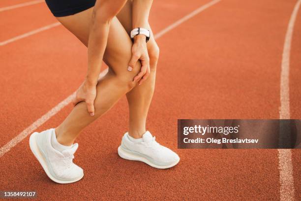 woman hurted ankle on running sports track. spasm and pain, female health problems in professional sports - sehnenscheidenentzündung stock-fotos und bilder