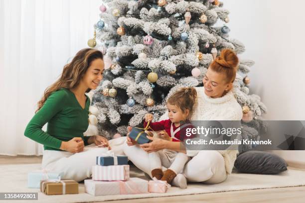 happy family with christmas gift near decorated christmas tre. - glamourous granny stock pictures, royalty-free photos & images