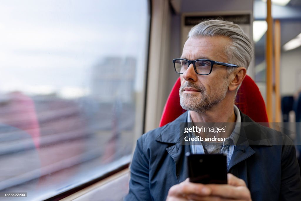 Nachdenklicher Mann, der sein Telefon benutzt, während er in einem Zug fährt