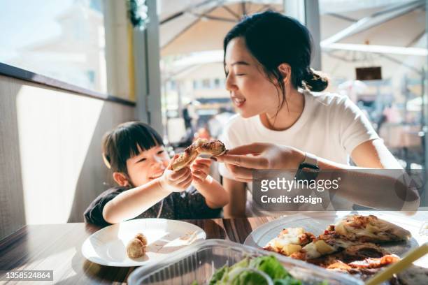 joyful young asian mother and lovely little daughter having lunch, eating freshly served pizza in restaurant. family enjoying bonding time and a happy meal together. family and eating out lifestyle - family dining stockfoto's en -beelden