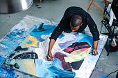 Busy black man drawing lines on a big canvas with painting on a table