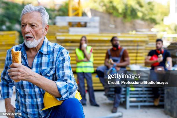 senior construction worker is taking a break and eating. - lunchpauze stockfoto's en -beelden
