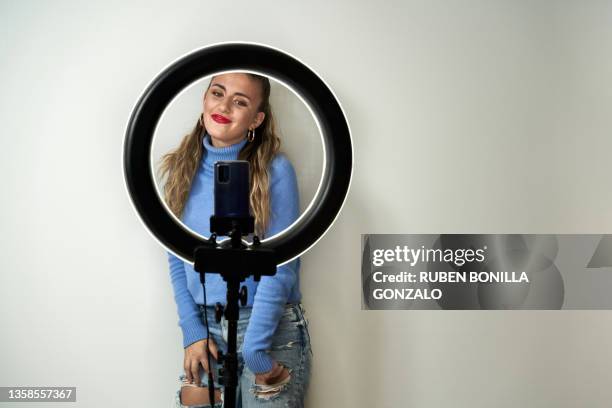 young blonde caucasian teenager influencer recording a video with smart phone in ring light on white background. - celebrity connected foto e immagini stock