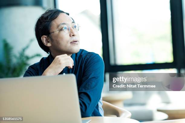 japanese entrepreneur using a laptop and thinking about business plan in a remote office.  business minded entrepreneurship. - asian man thinking stock-fotos und bilder