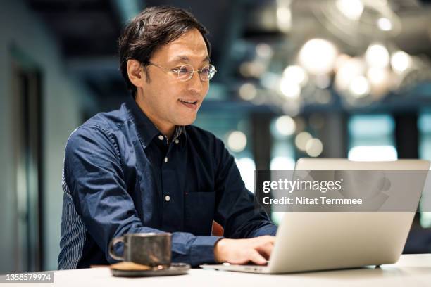 technology drives business growth. japanese businessman typing and replying email by a laptop to his customer in the office space. - businessman working on a laptop with a coffee stock-fotos und bilder