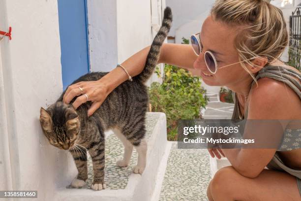 une jeune femme câline un chat errant en grèce - ile d'ios grèce photos et images de collection