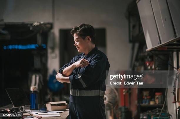 asian chinese female workshop owner rolling sleeve getting ready to work at workbench - rolling up sleeve stock pictures, royalty-free photos & images