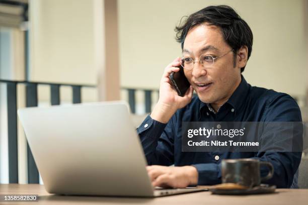 thoughtful japanese businessman discussion with a business partner on a cell phone and looking business report on a laptop in a modern office. business communication with technology. - 40代 男性 ストックフォトと画像