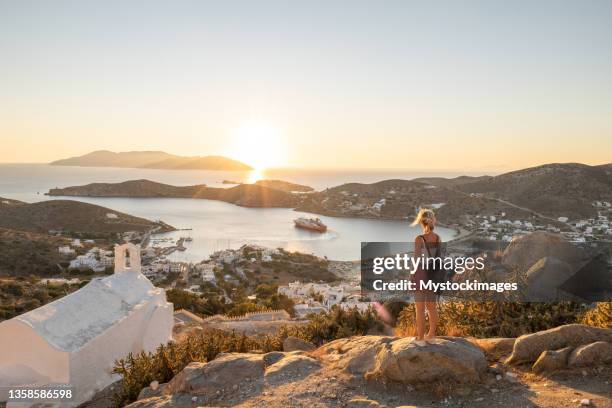 woman on cliff looks across sea at sunset, greek town view - ios greece stock pictures, royalty-free photos & images