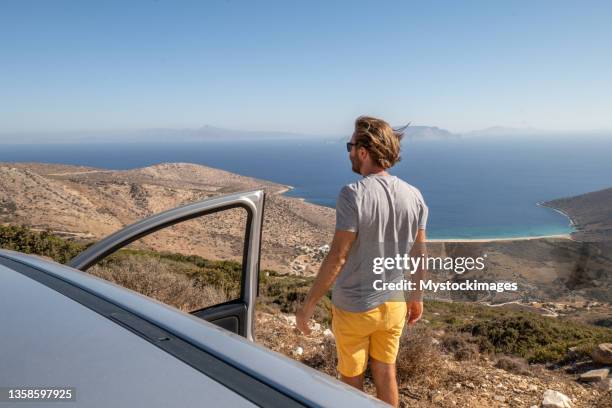 young man get out of the car to look at panorama, beach view road trip concept - ios grécia imagens e fotografias de stock