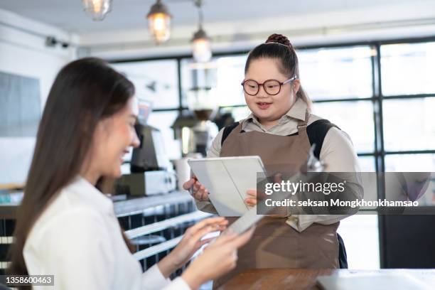 asian woman with down syndrome taking orders in the coffee shop - gelijkwaardige behandeling stockfoto's en -beelden