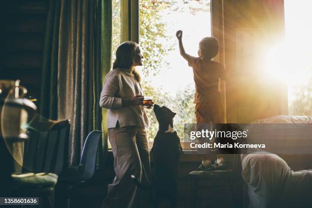 mother and little son drawing on window at home - happy woman in early morning sunlight stock-fotos und bilder