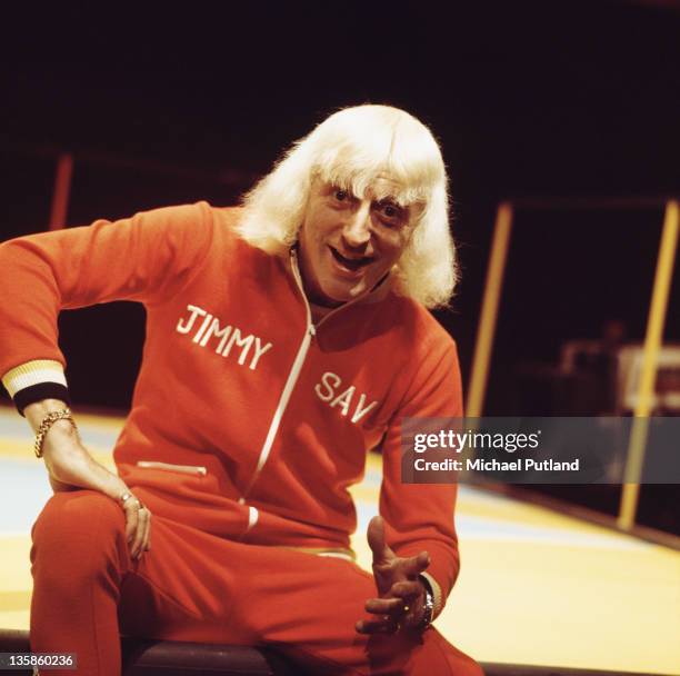 English disc jockey Jimmy Savile presenting the BBC music chart show 'Top Of The Pops', UK, circa 1973. He is wearing a personalised tracksuit.