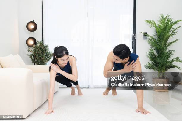 happy asian couple doing exercise together in living room at home. sporty woman and man smile and make exercise indoors daily routine while social distancing. home fitness concept. - friends social distancing stock pictures, royalty-free photos & images