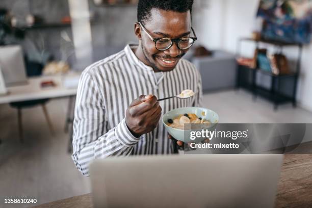 man eating breakfast and using laptop - eating cereal stock pictures, royalty-free photos & images