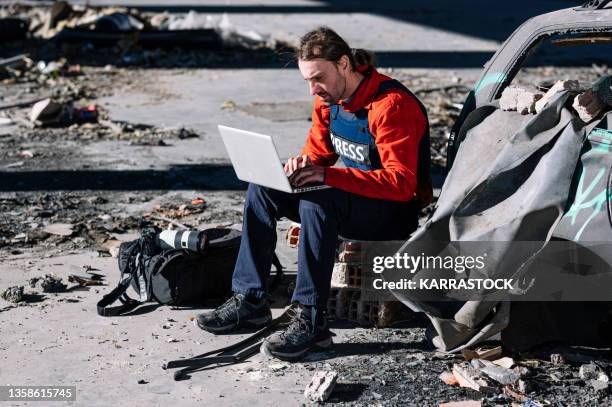 a man, a war journalist with a laptop and digital camera at the scene of the action, in a war zone. - conflict zone stock pictures, royalty-free photos & images