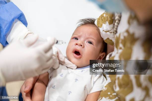 newborn baby boy taking the rotavirus oral vaccine in a hospital held by his mother - baby being held stockfoto's en -beelden