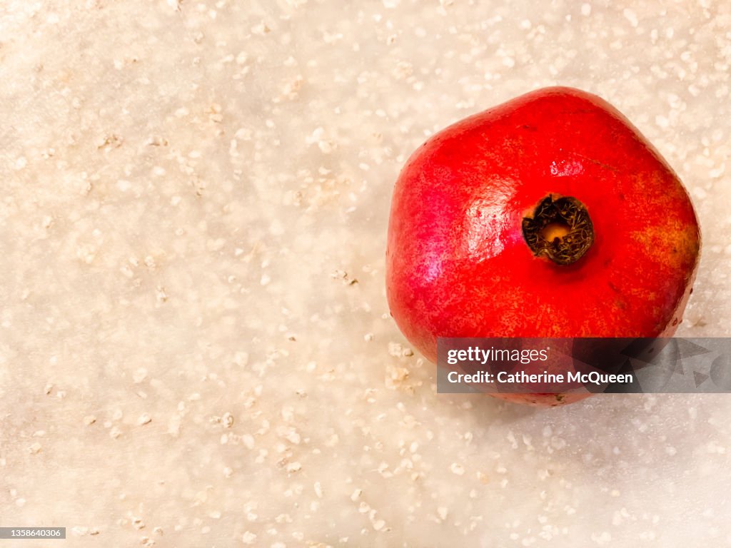 Fresh whole bright red pomegranate against white cutting board background