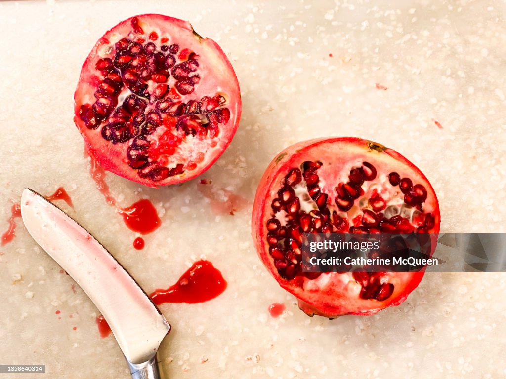 Fresh sliced pomegranate beside kitchen knife against white cutting board background