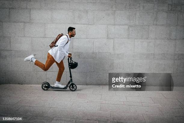 man riding push scooter in city street - scooter stock pictures, royalty-free photos & images