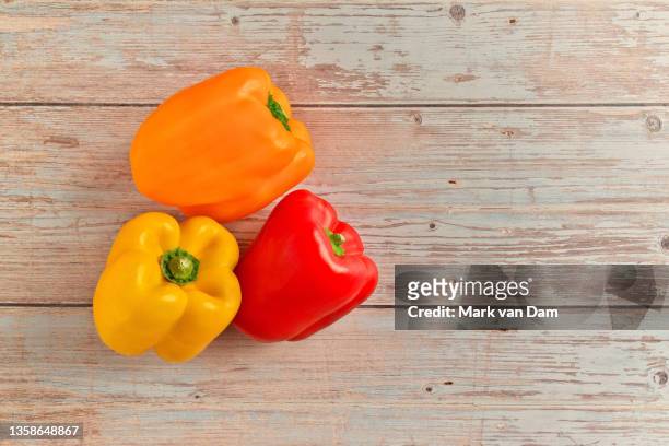 studio shot of red, orange and yellow bell peppers on a rustic wood table - yellow bell pepper stock-fotos und bilder