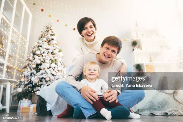 happy young family with a baby is taking a timer selfie in their living room decorated for christmas and new year holidays - happy holidays family stock pictures, royalty-free photos & images