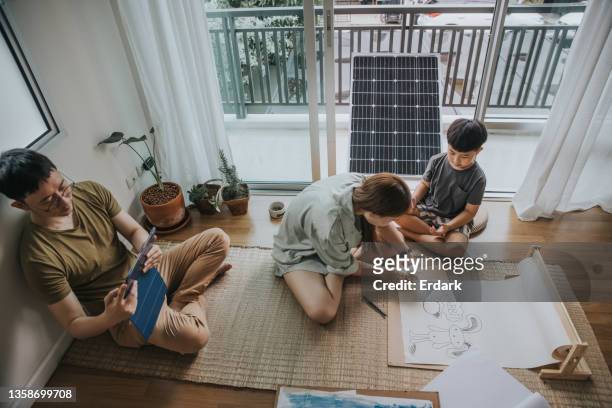 junge asiatin und ihr sohn spielen mit kaninchen, während der vater zu hause an einem tablet arbeitet - stockfoto - fuel and power generation stock-fotos und bilder