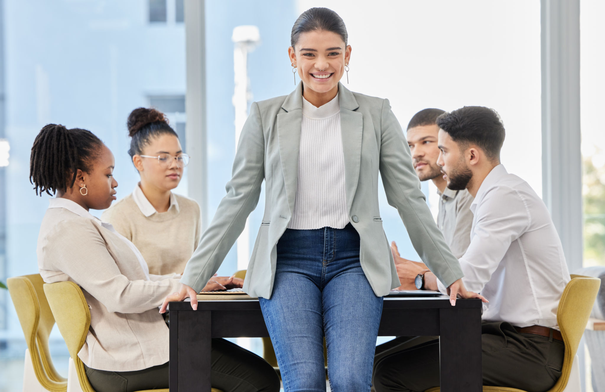 Portrait of a young businesswoman standing in an office while her colleagues have a meeting in the background Portrait of a young businesswoman standing in an office while her colleagues have a meeting in the background