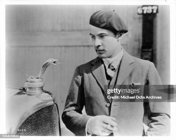 Rudolph Valentino is looking at a snake on hood of car, 1925.